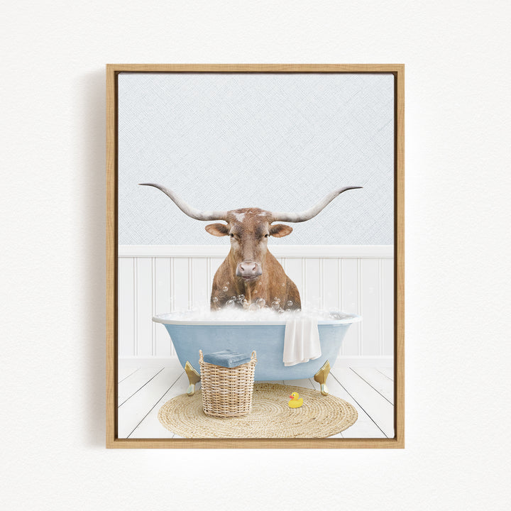 A brown cow with long horns is sitting in a blue bathtub filled with water, surrounded by a basket of toys and a yellow rubber duck.