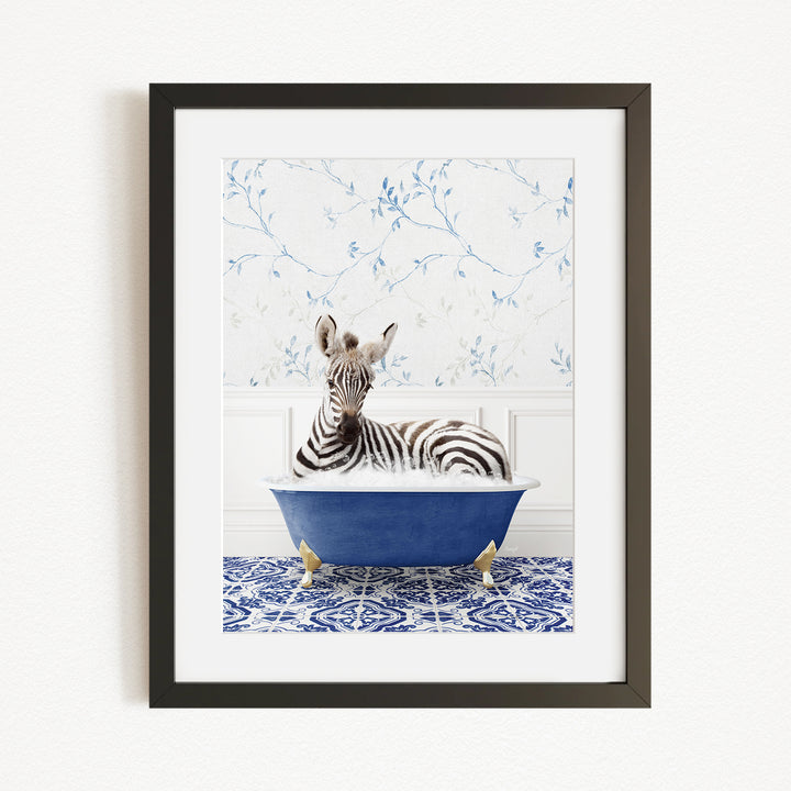 A zebra is sitting in a blue bathtub, surrounded by a blue and white patterned rug and a white wall with blue floral wallpaper.