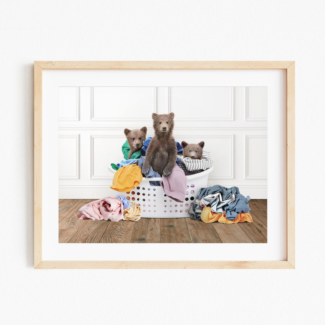 A framed image depicting three bears sitting on a pile of laundry, with various clothes and blankets surrounding them.