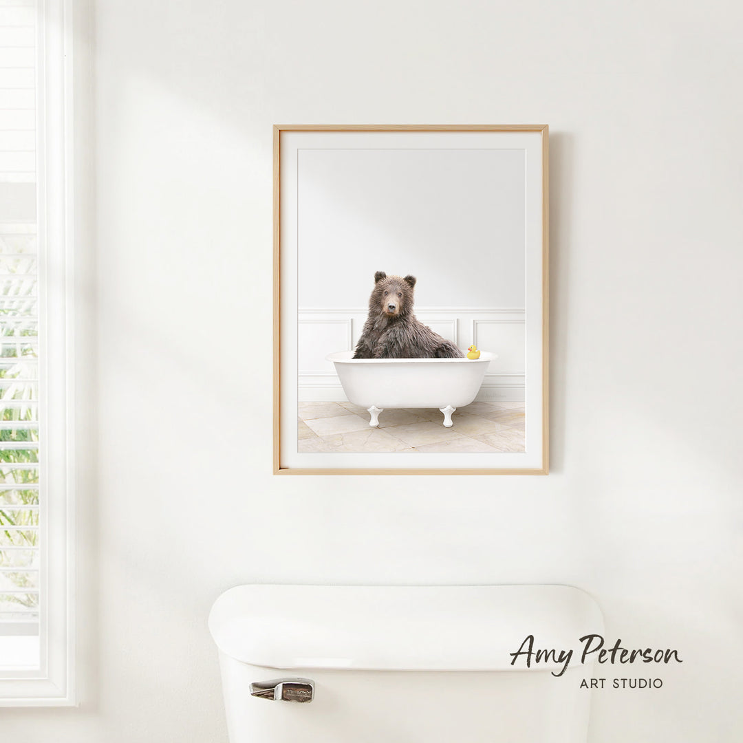 A framed image of a bear sitting in a bathtub, with a yellow rubber duck floating on the water.