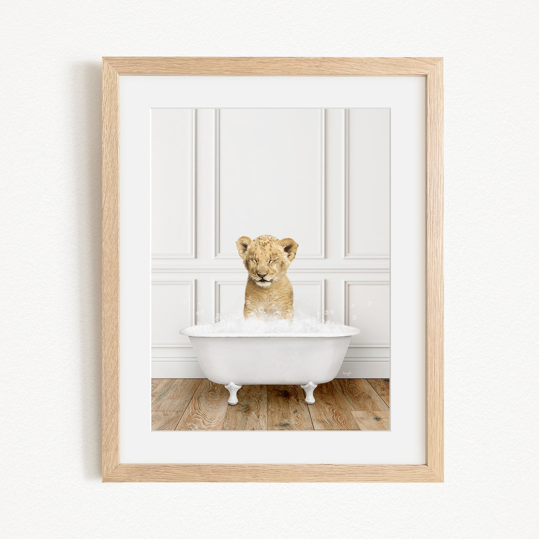 A young lion cub sitting in a white bathtub filled with water, surrounded by a wooden floor.