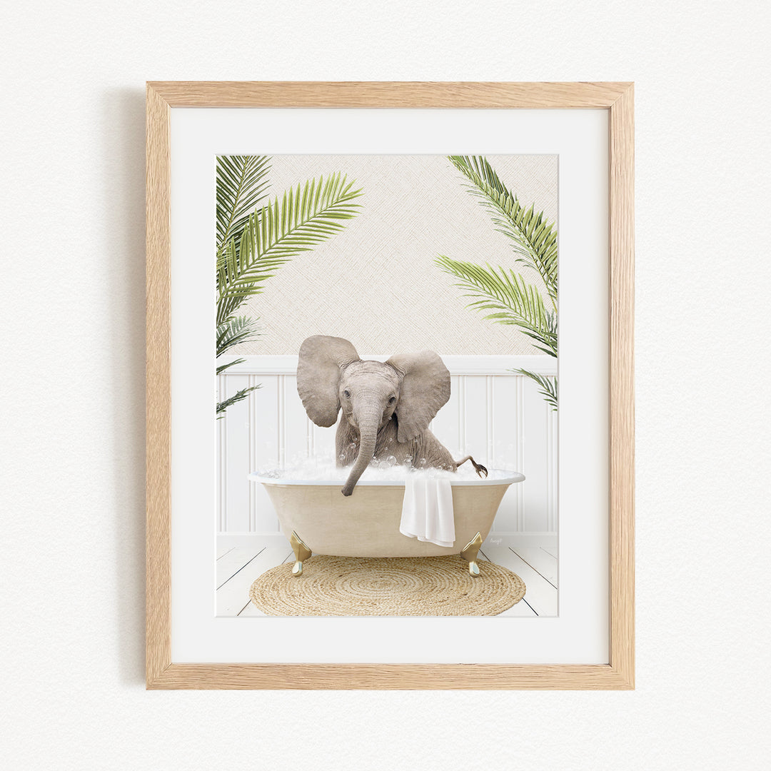 A framed image of a baby elephant sitting in a bathtub filled with water, surrounded by palm leaves.