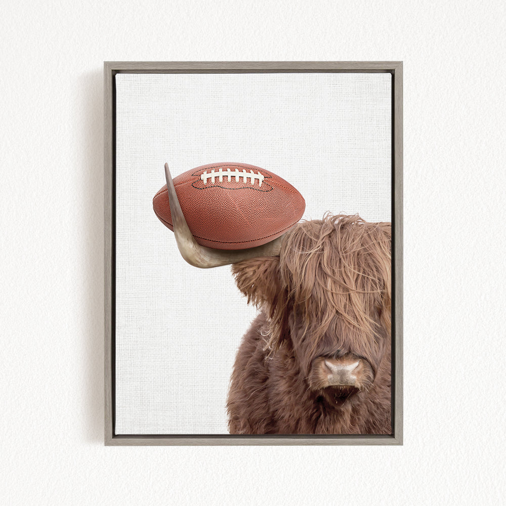 A framed image of a Highland cow with a football resting on its head.