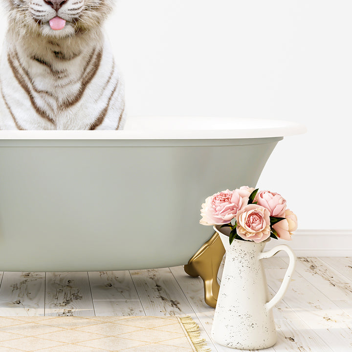 A white tiger is sitting in a green bathtub, with a vase of pink flowers next to it on a wooden floor.