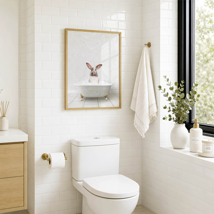 A bathroom with a white toilet, a framed picture of a rabbit in a bathtub, and a window with greenery on the sill.