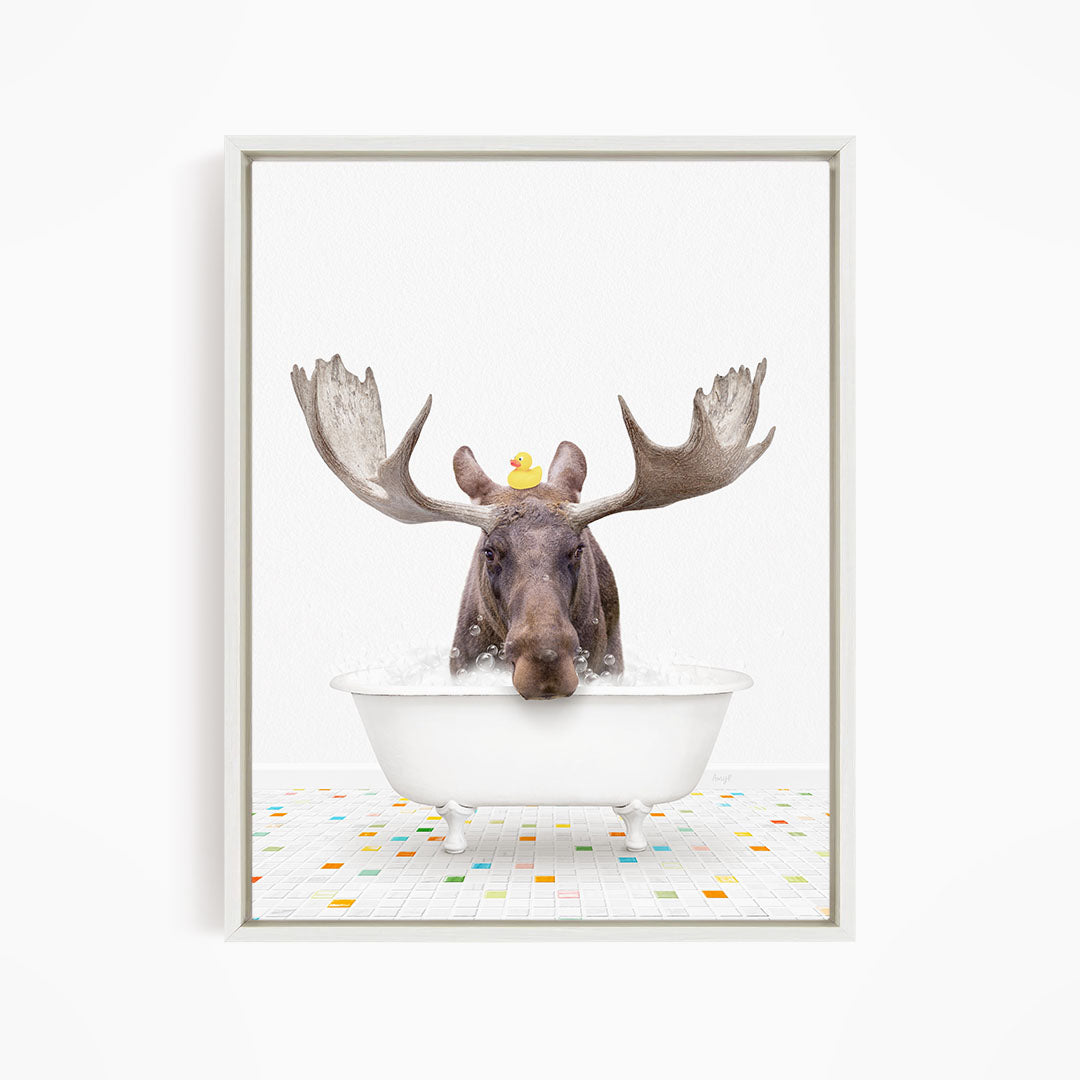 A moose with large antlers is sitting in a white bathtub, with a rubber duck perched on its head.