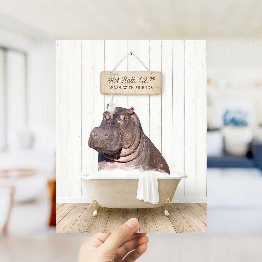 A hand holding a framed image of a hippopotamus sitting in a bathtub, with a sign above it that says "Hot Bath $2.00 WASH WITH FRIENDS".