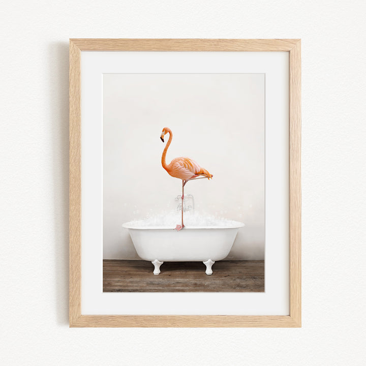 A framed image of a flamingo standing on one leg inside a white bathtub filled with water.