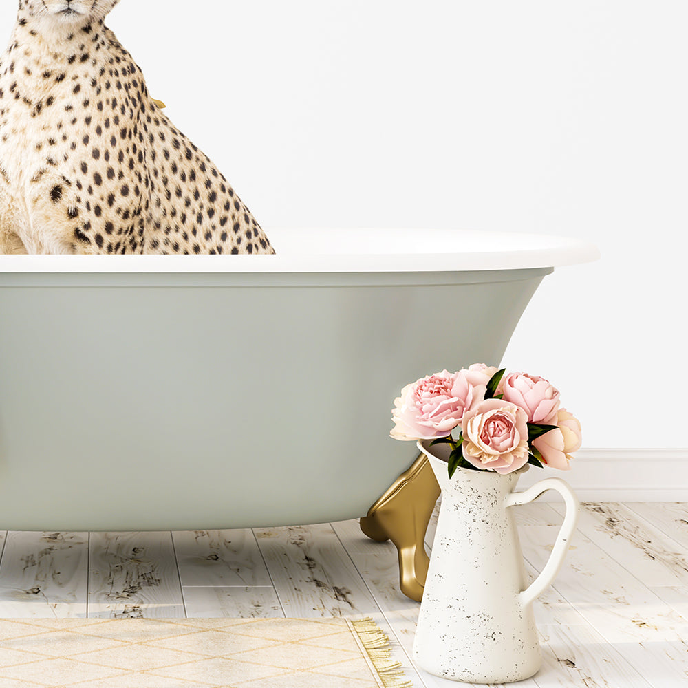 A leopard-spotted cat sits in a green bathtub, with a white vase filled with pink flowers placed next to it on a wooden floor.