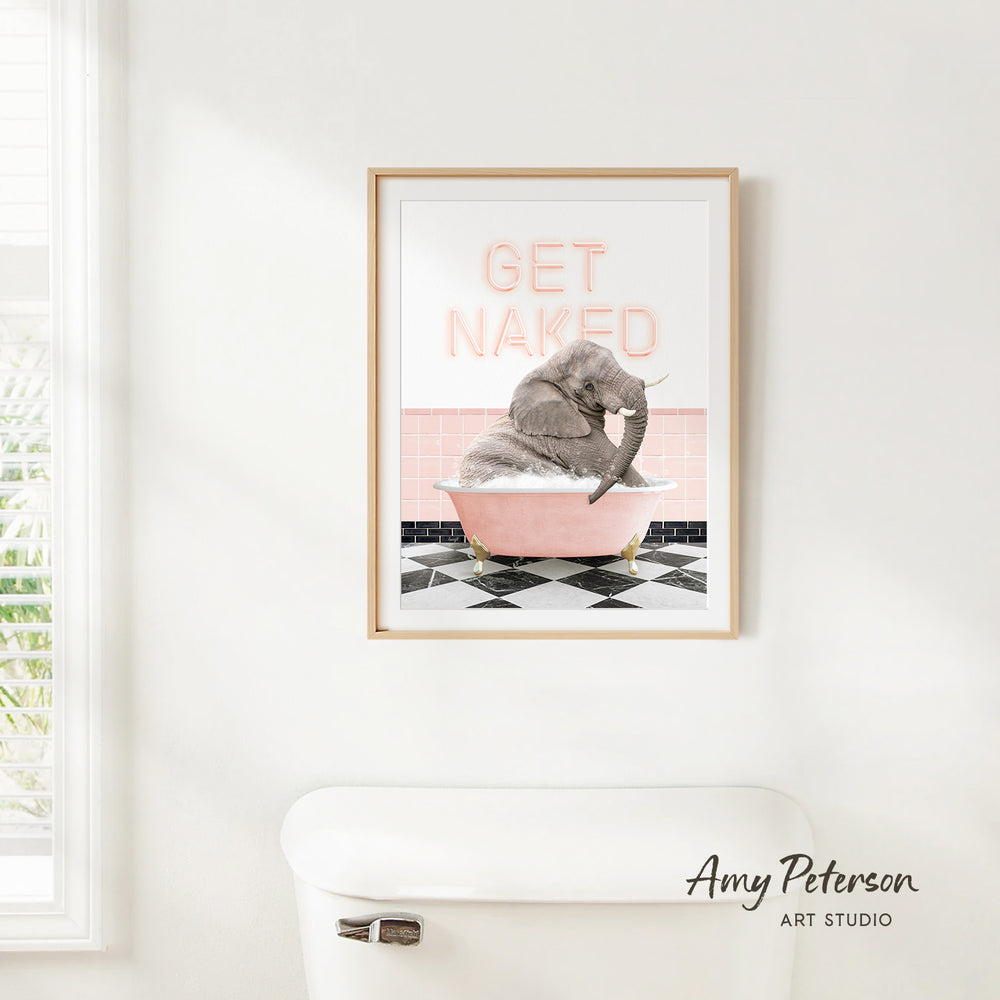 A framed print of an elephant sitting in a pink bathtub with the text "GET NAKED" on it, hanging on a white wall.
