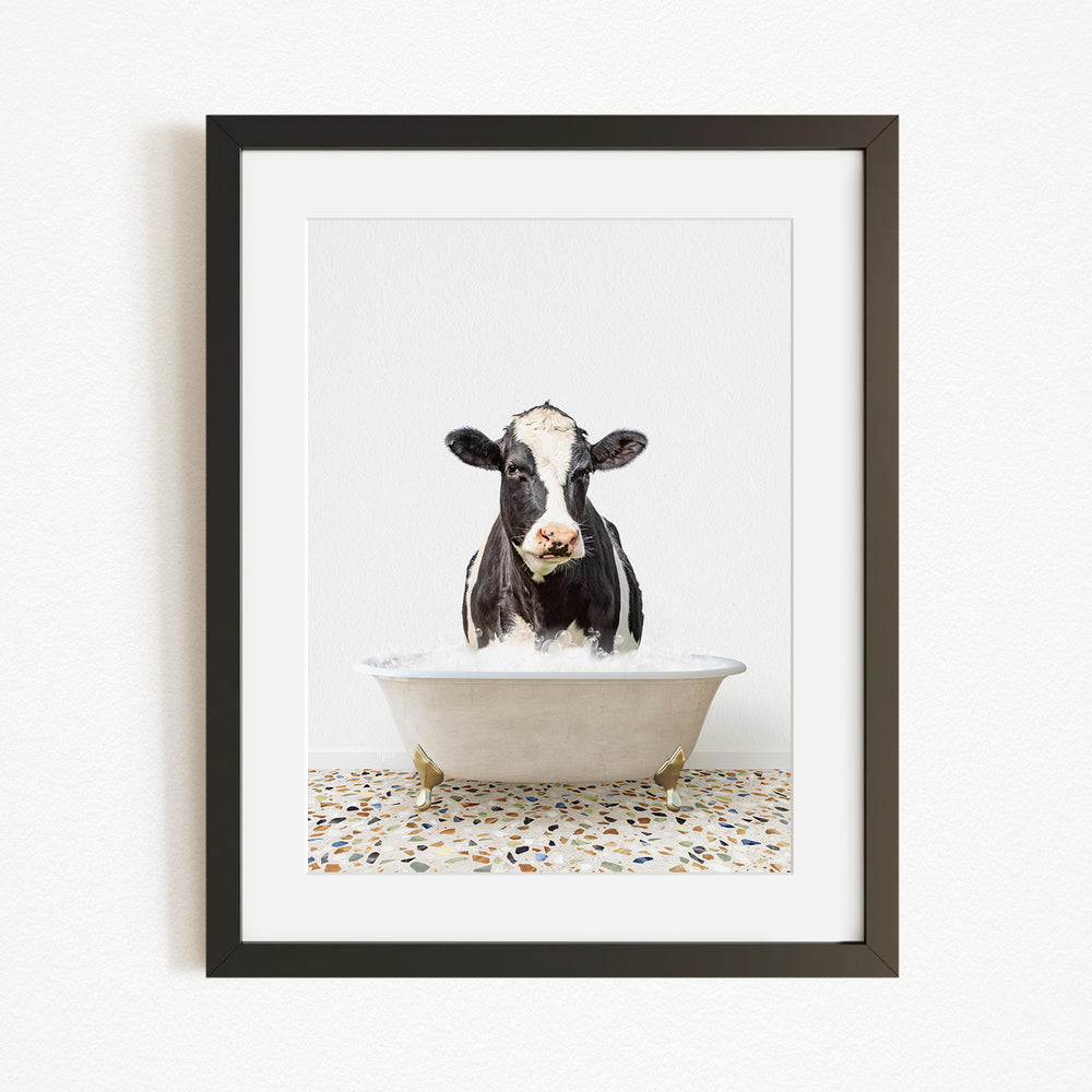 A black and white cow is sitting in a white bathtub filled with water, creating a whimsical and humorous scene.