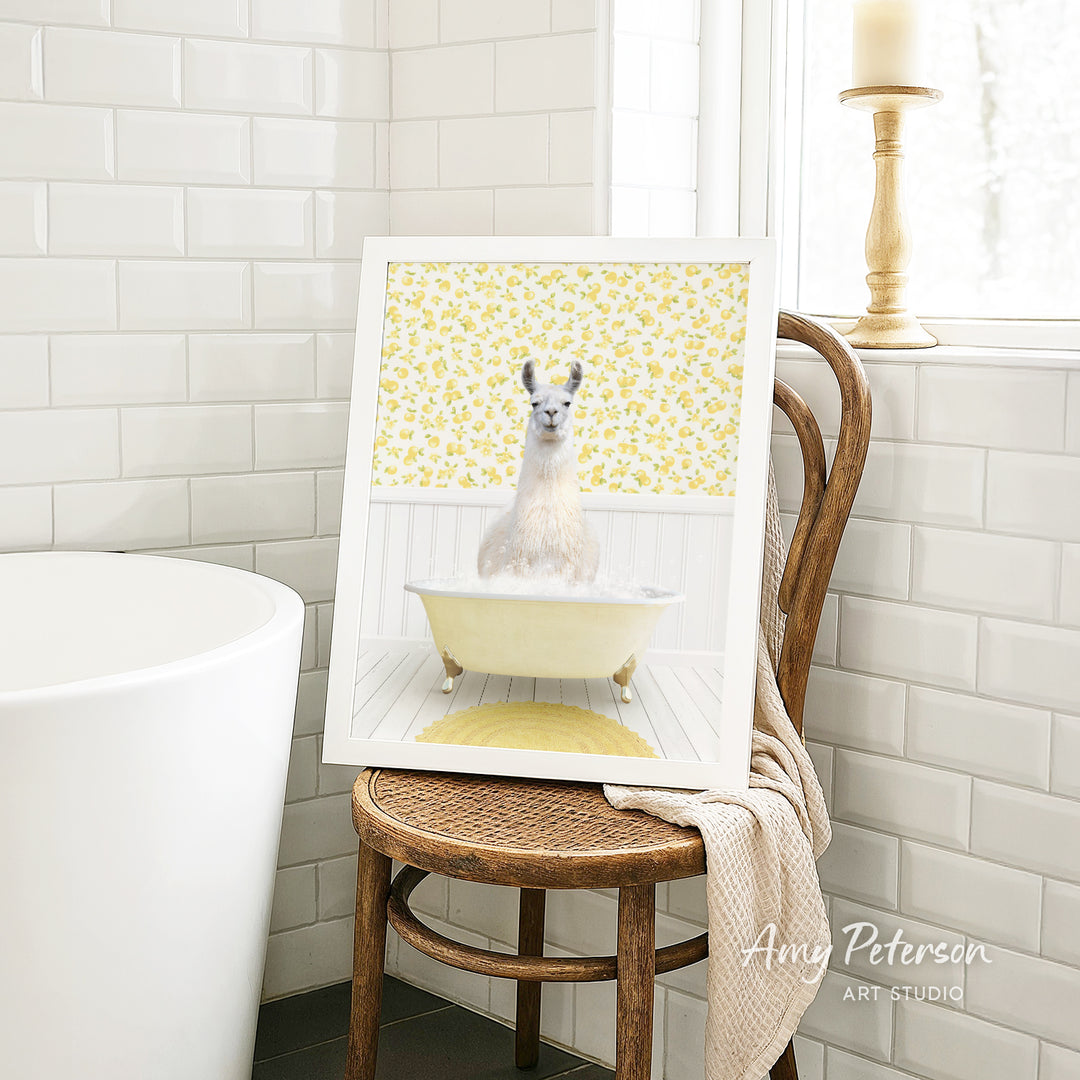 A framed image of a white llama sitting in a yellow bathtub, with a yellow floral pattern on the wall behind it.