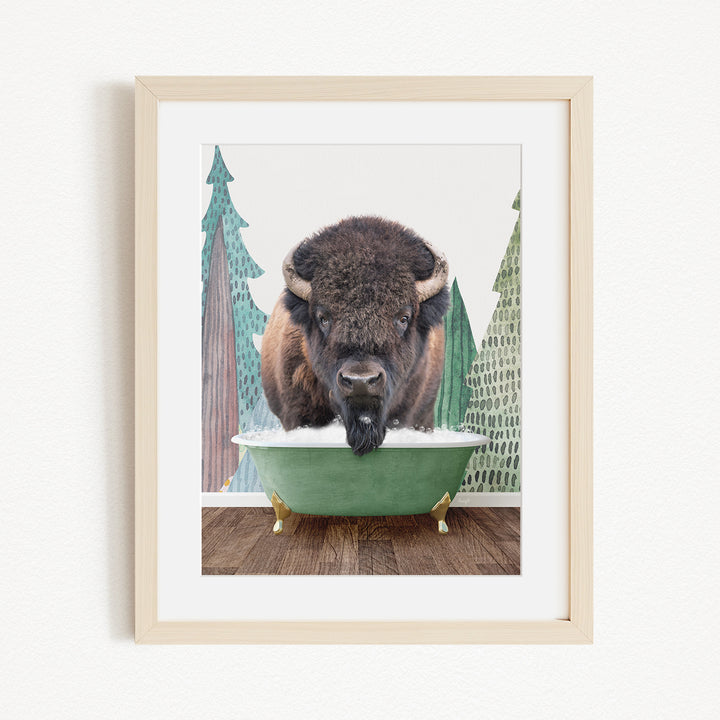 A bison is standing in a green bathtub, with a snowy landscape and pine trees in the background.