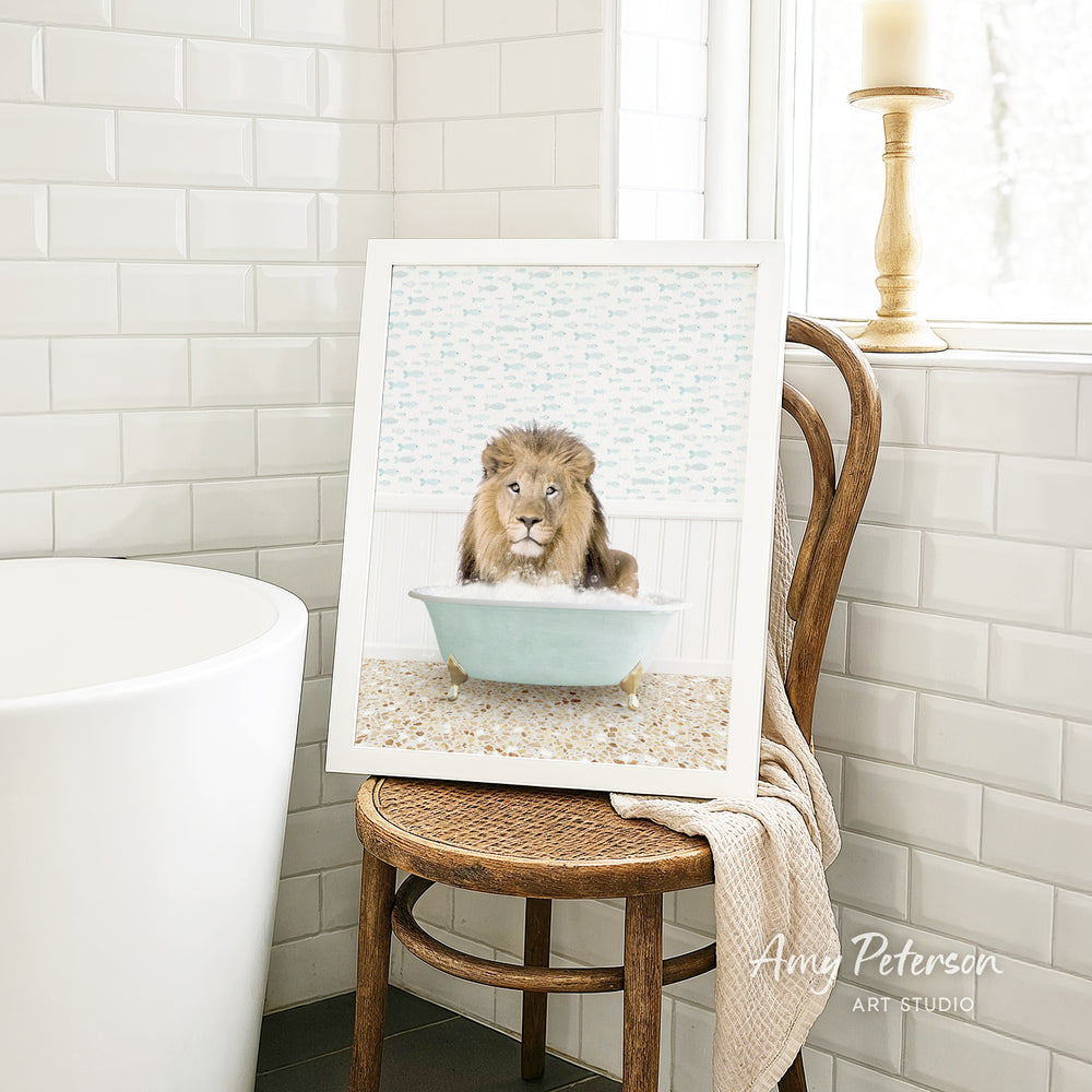 A framed image of a lion sitting in a bathtub, with a towel draped over the back of a chair in a bathroom setting.