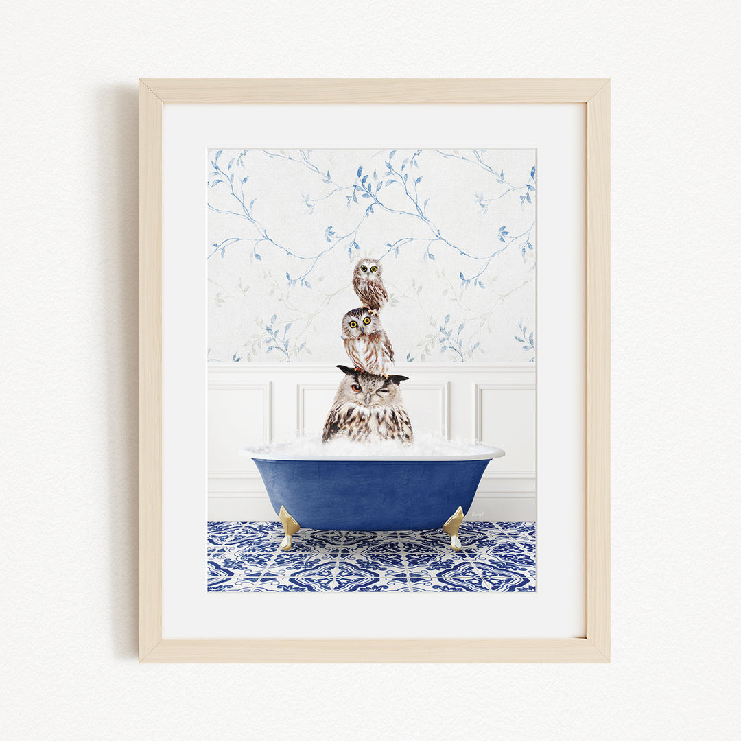 A framed image depicting a group of owls sitting in a blue bathtub, with a patterned tile floor and a floral wallpaper in the background.