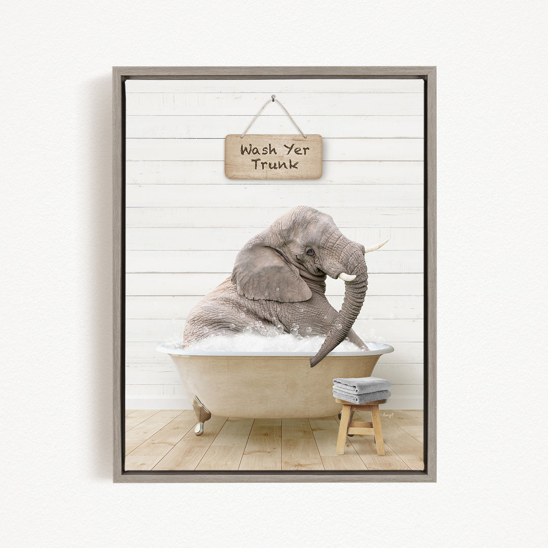 A gray elephant is sitting in a bathtub filled with water, with a sign above it that says "Wash Yer Trunk".