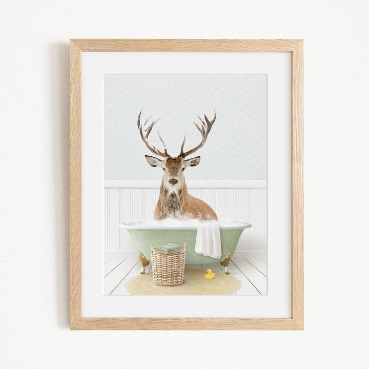 A deer with antlers is sitting in a green bathtub filled with water, surrounded by a basket of rubber ducks and a yellow rubber ducky.