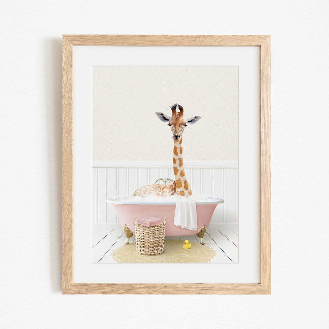 A giraffe sitting in a pink bathtub filled with bubbles, surrounded by a yellow rubber duck and a basket.