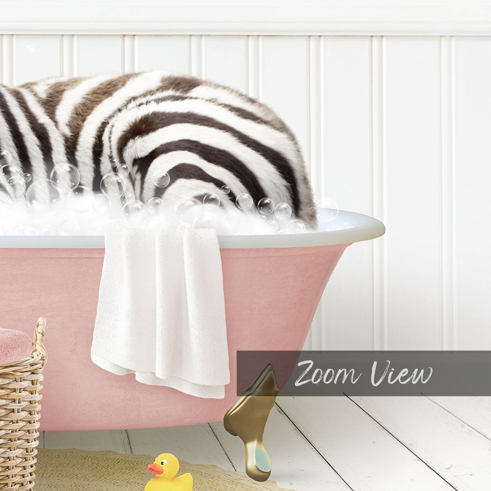 A zebra lying in a pink bathtub filled with bubbles, surrounded by a yellow rubber duck and a white basket.