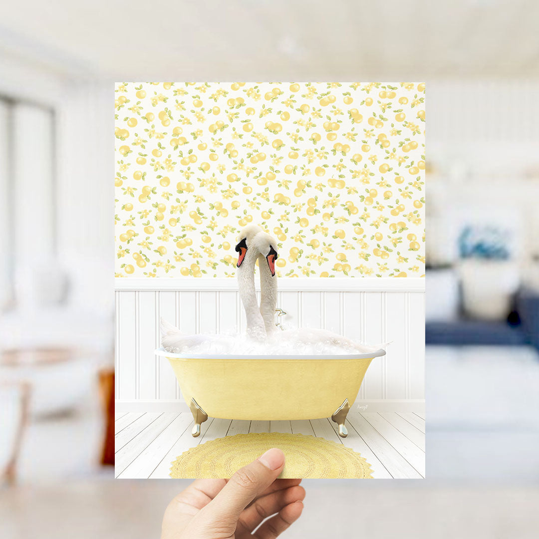 A hand holds up a framed photograph of a swan sitting in a yellow bathtub, surrounded by a yellow and white floral pattern on the wall.