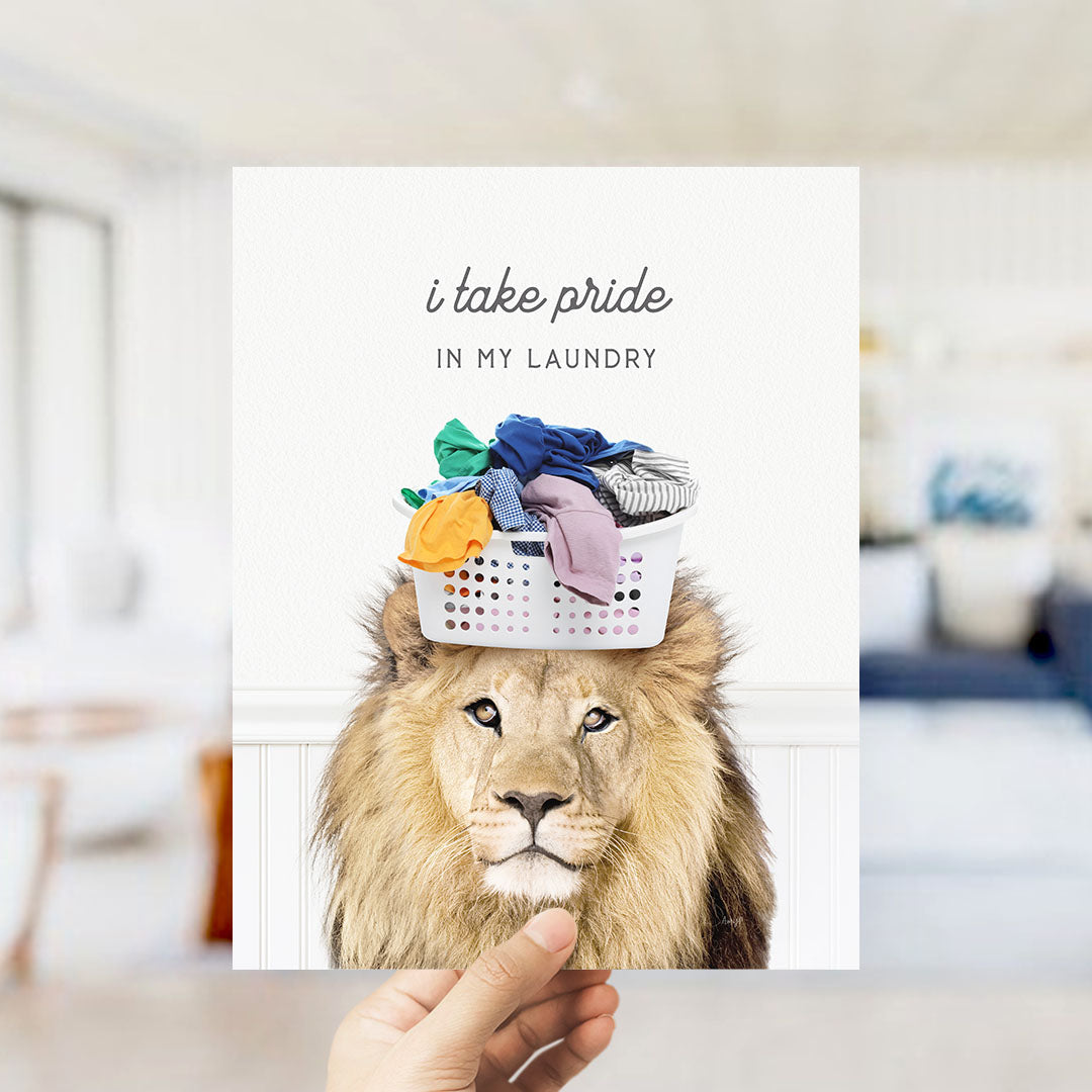 A hand holding a card with a lion's head wearing a laundry basket on its head, with the text "I take pride in my laundry" written above it.