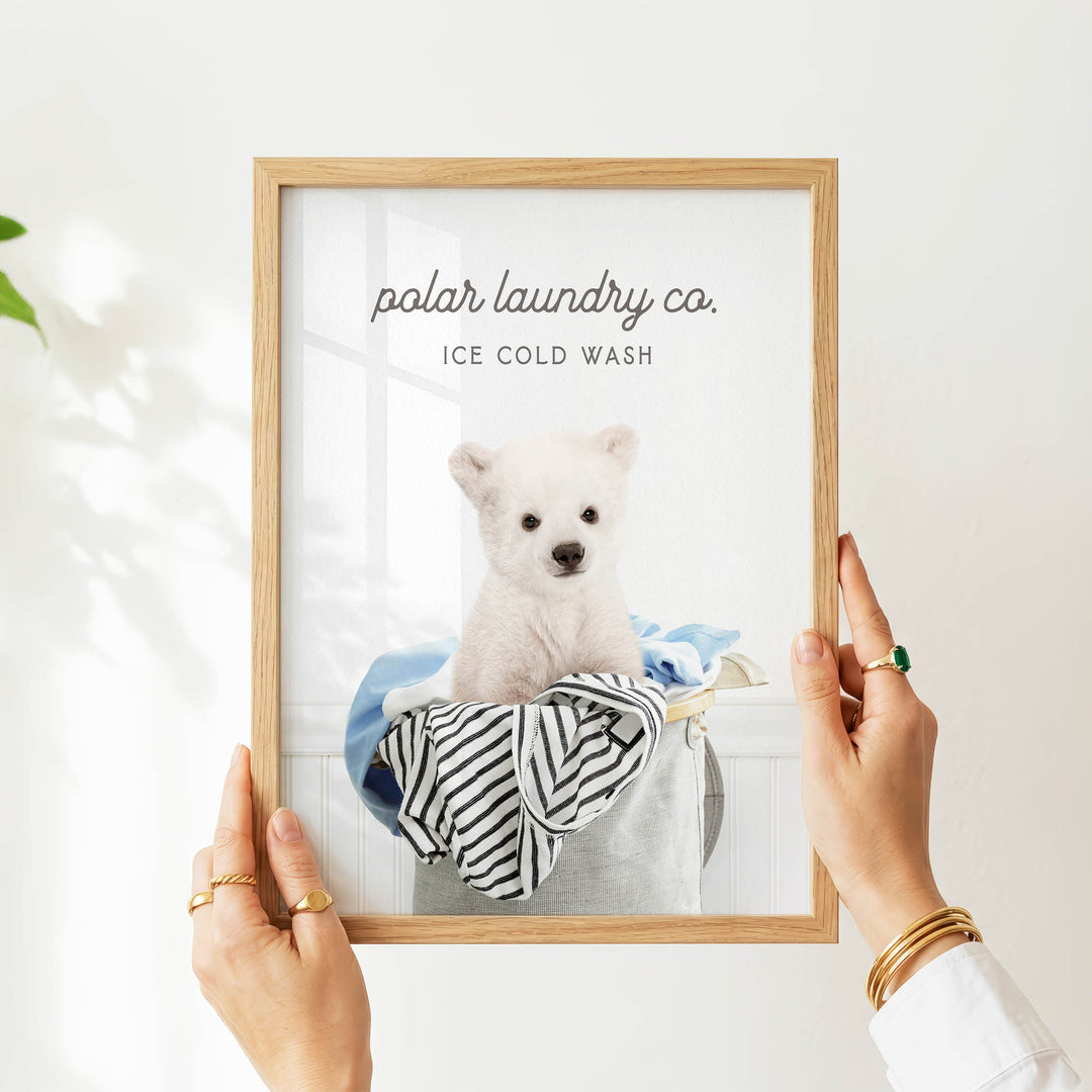 A person is holding up a framed image of a white polar bear sitting in a laundry basket, with the text "polar laundry co. ICE COLD WASH" displayed on the frame.