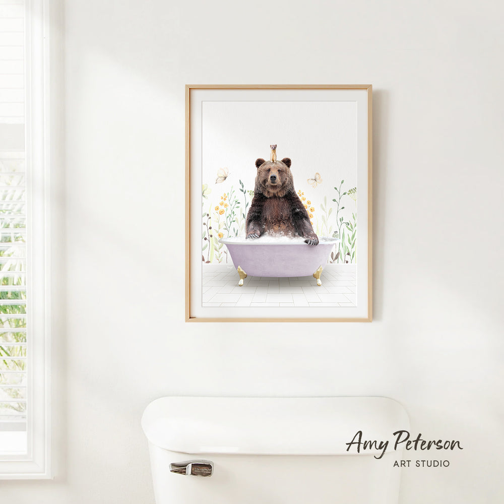 A framed print of a bear sitting in a bathtub is hanging on a white wall.