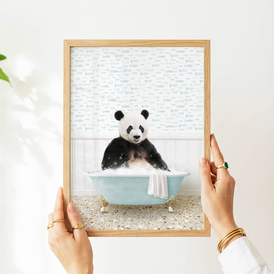A person's hands are holding a framed picture of a panda bear sitting in a bathtub filled with bubbles.