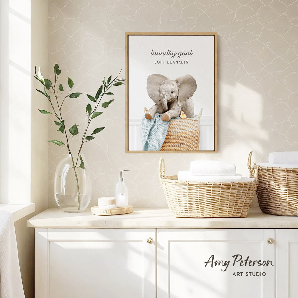 a framed poster of an elephant sitting in a basket, hanging on a wall above a white cabinet with baskets.