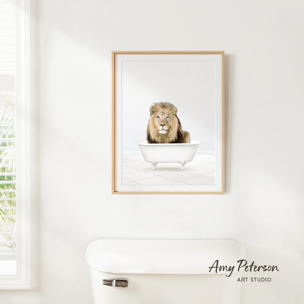 A framed image of a lion sitting in a bathtub is hanging on a white wall.