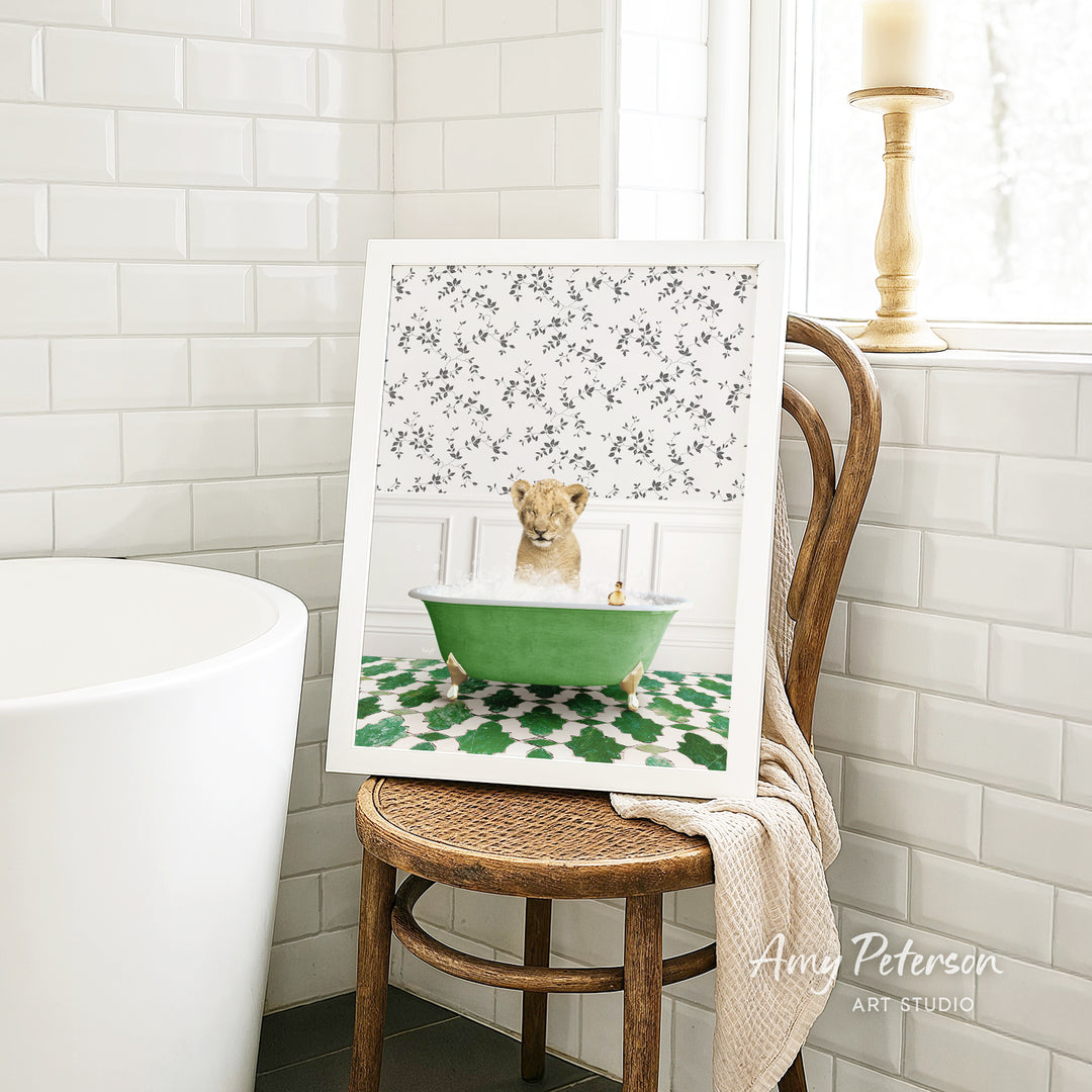 A framed image of a lion sitting in a green bathtub, surrounded by a floral pattern, is displayed on a wooden chair in a bathroom setting.
