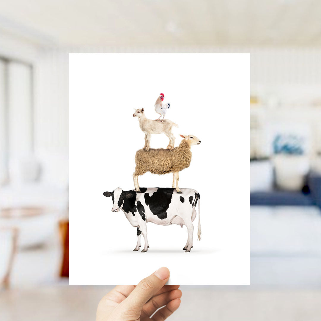 A hand is holding up a white card with an illustration of a cow, sheep, and chicken stacked on top of each other.
