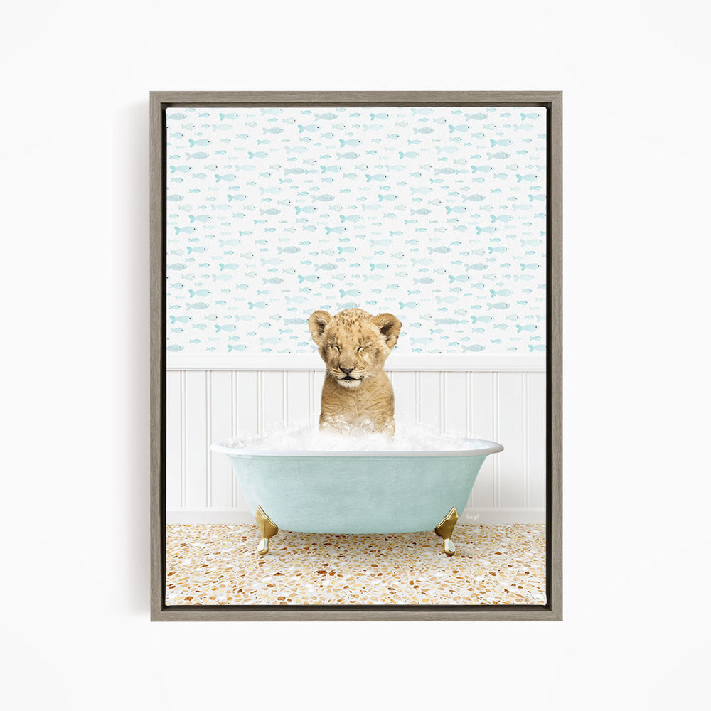 A young lion cub sitting in a blue bathtub filled with water, surrounded by a pattern of fish.