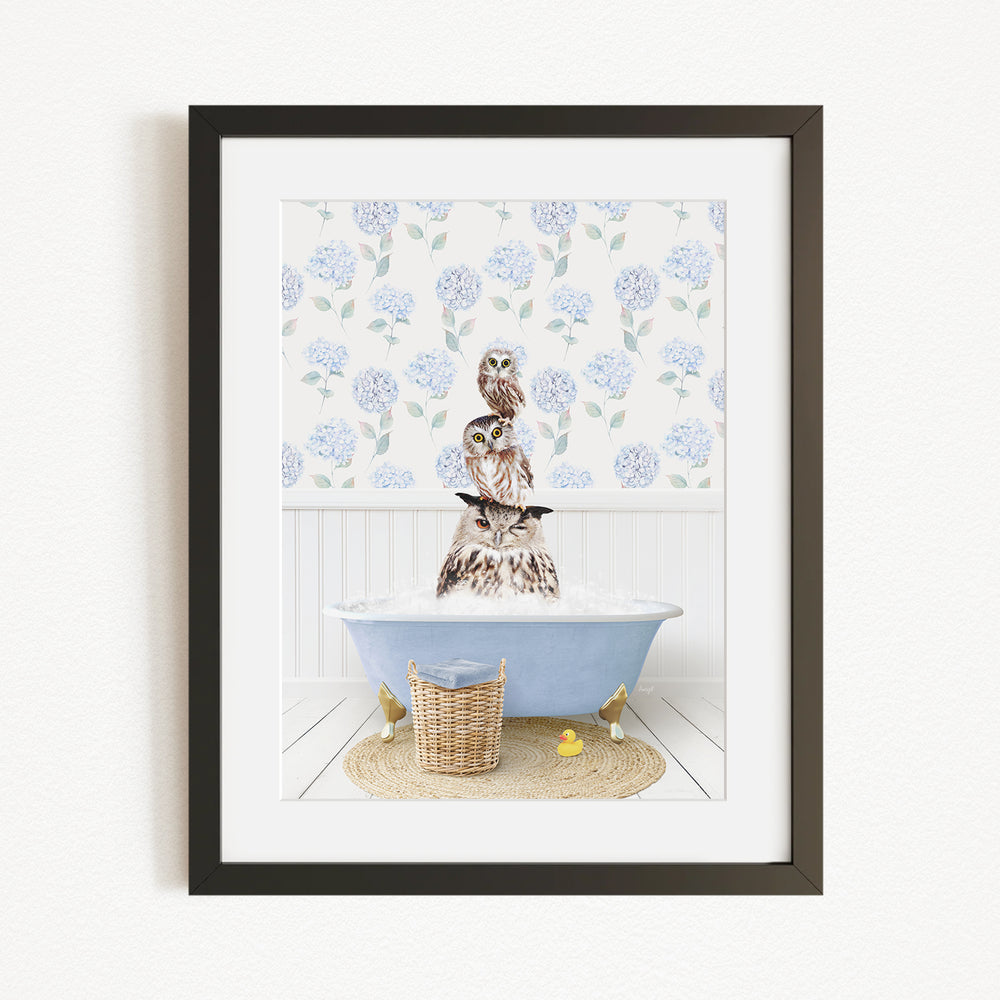A framed image depicting a brown owl sitting on a blue bathtub filled with water, surrounded by a white floral pattern on the wall behind it.