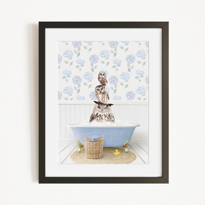 A framed image depicting a brown owl sitting on a blue bathtub filled with water, surrounded by a white floral pattern on the wall behind it.