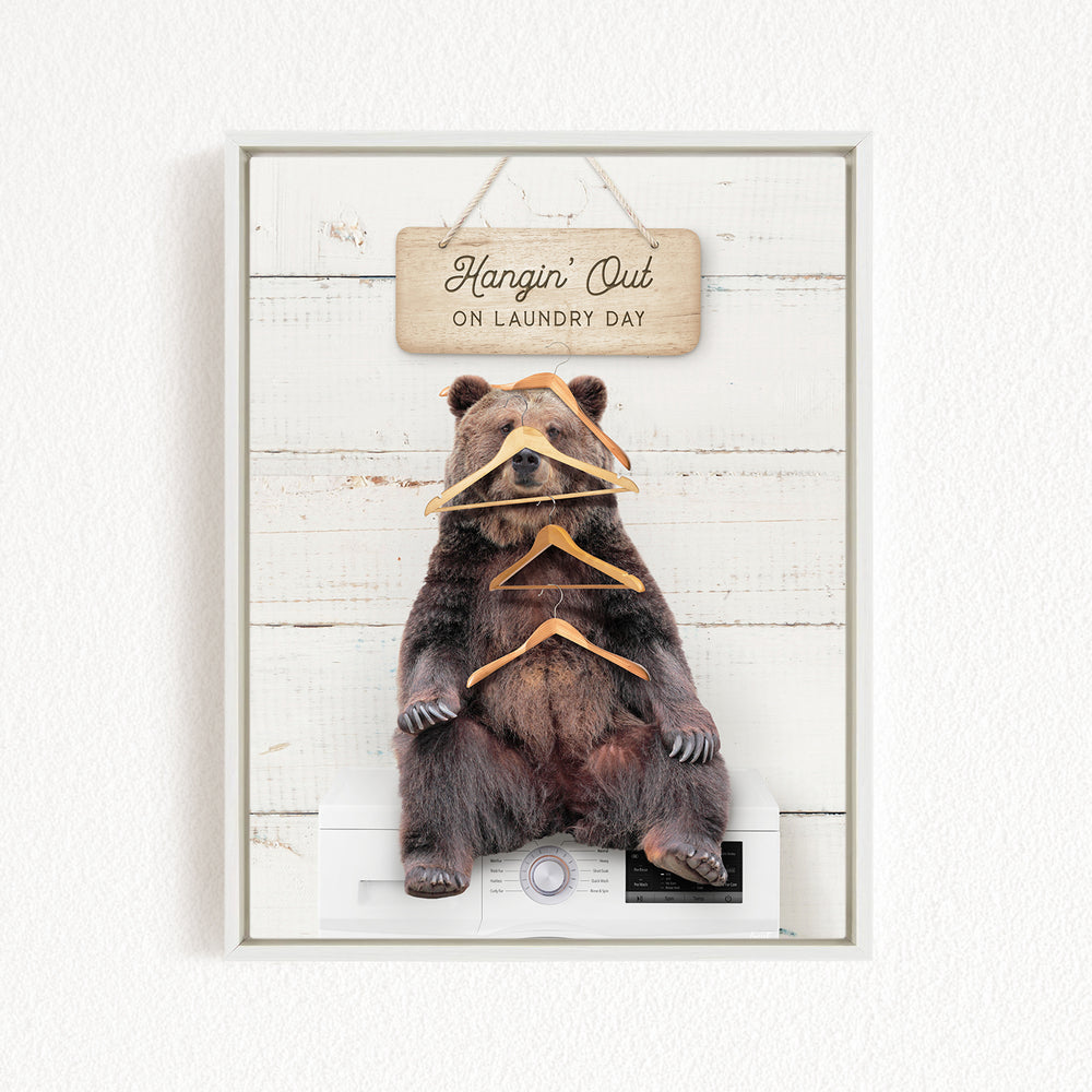 A framed image of a brown bear sitting on a white washing machine, with a wooden sign above it that says "Hangin' Out on Laundry Day".