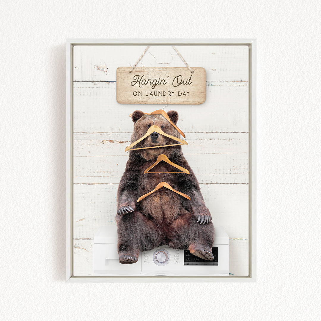 A framed image of a brown bear sitting on a white washing machine, with a wooden sign above it that says "Hangin' Out on Laundry Day".