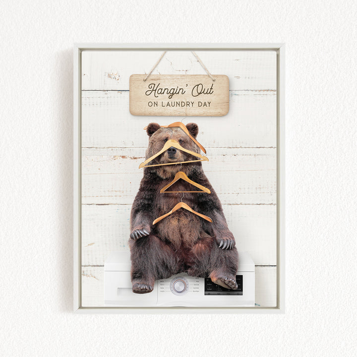 A framed image of a brown bear sitting on a white washing machine, with a wooden sign above it that says "Hangin' Out on Laundry Day".