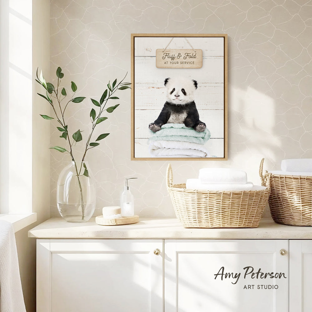 a framed picture of a panda bear sitting on a towel, hanging on a wall above a white cabinet with baskets.