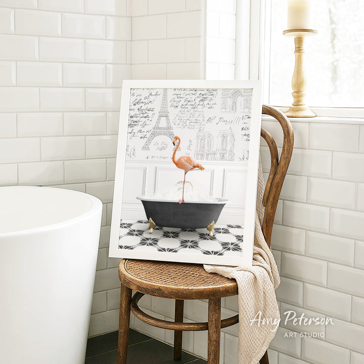 A framed image of a pink flamingo standing in a bathtub, with a tiled floor and a window in the background.
