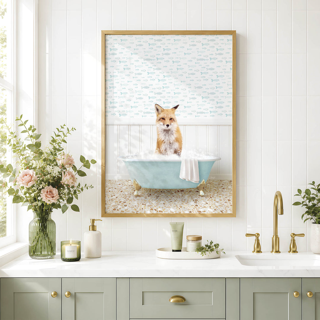 A framed image of a fox sitting in a bathtub, surrounded by flowers and greenery, is displayed on a white tiled wall above a bathroom counter with various toiletries and a plant.