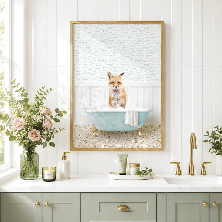 A framed image of a fox sitting in a bathtub, surrounded by flowers and greenery, is displayed on a white tiled wall above a bathroom counter with various toiletries and a plant.