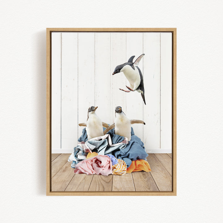 A framed image depicting two penguins standing on a pile of clothes, with one penguin flying in the air above the other.