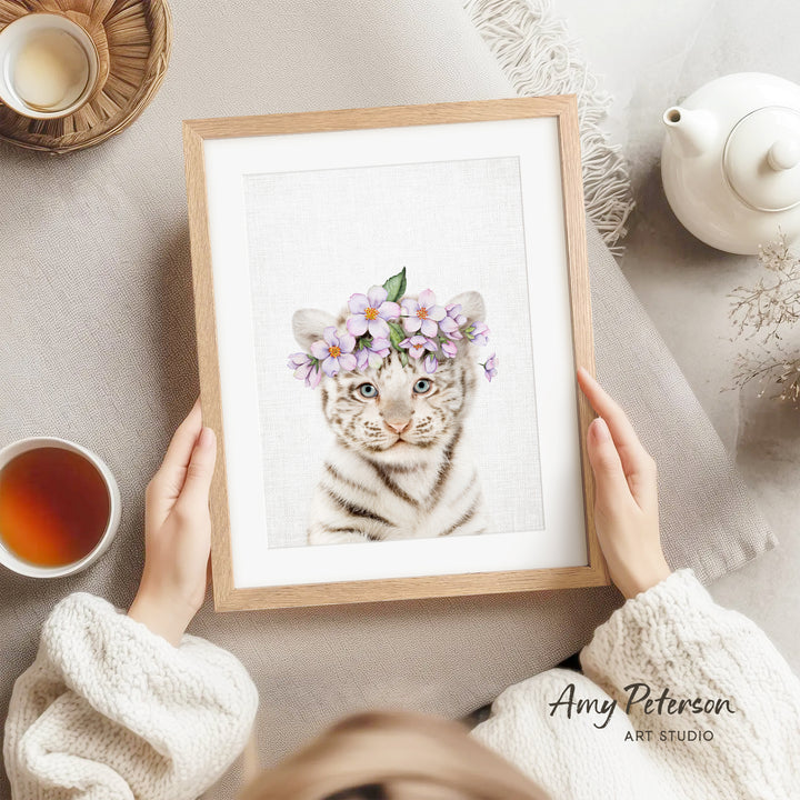A person is holding a framed picture of a tiger wearing a flower crown, with a teapot, a cup of tea, and a bowl of tea visible in the background.