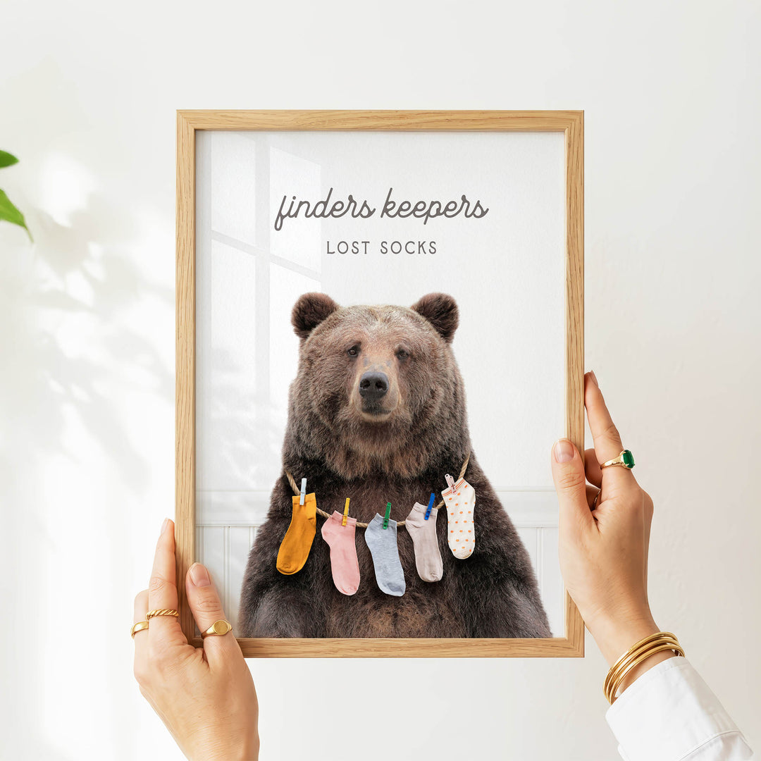 A person is holding up a framed image of a bear wearing socks, with the text "finders keepers" and "lost socks" written above the bear.