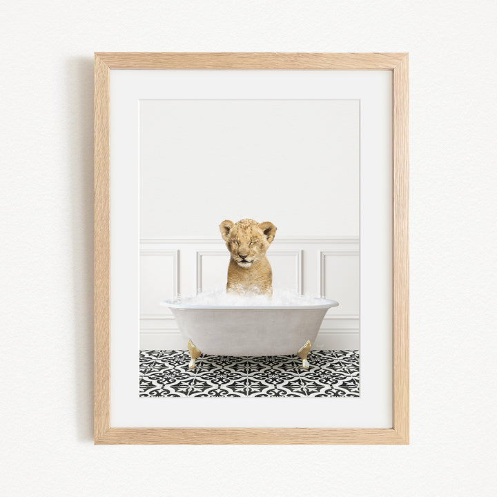 A young lion cub sitting in a white bathtub filled with water, surrounded by a black and white patterned floor.