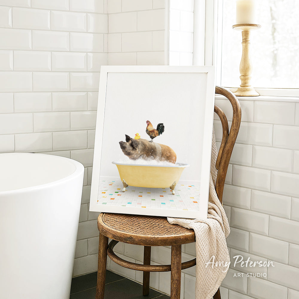 A framed image of a pig sitting in a yellow bathtub, with a rooster perched on its back, is displayed on a wooden chair in a bathroom setting.