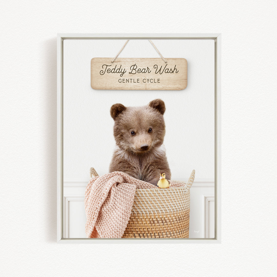 A teddy bear sitting in a woven basket, with a sign above that reads "Teddy Bear Wash Gentle Cycle".