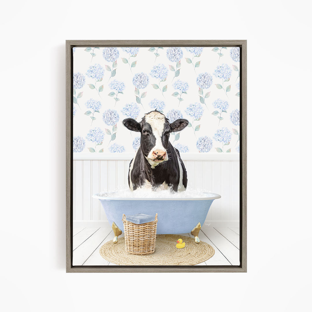 A black and white cow is sitting in a blue bathtub filled with water, surrounded by a wicker basket and rubber ducks.