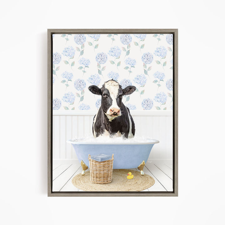 A black and white cow is sitting in a blue bathtub filled with water, surrounded by a wicker basket and rubber ducks.
